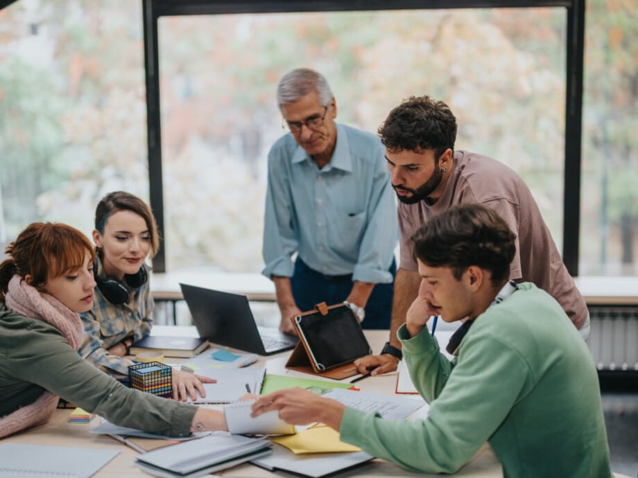 A group of university students working together on a project with their senior professor providing guidance and support. Collaborative learning and teamwork in an educational setting.